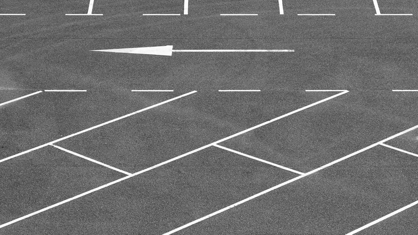 Yeni asfaltlanmış otoparkta beyaz park yeri çizgileri ve yönlendirme oku.